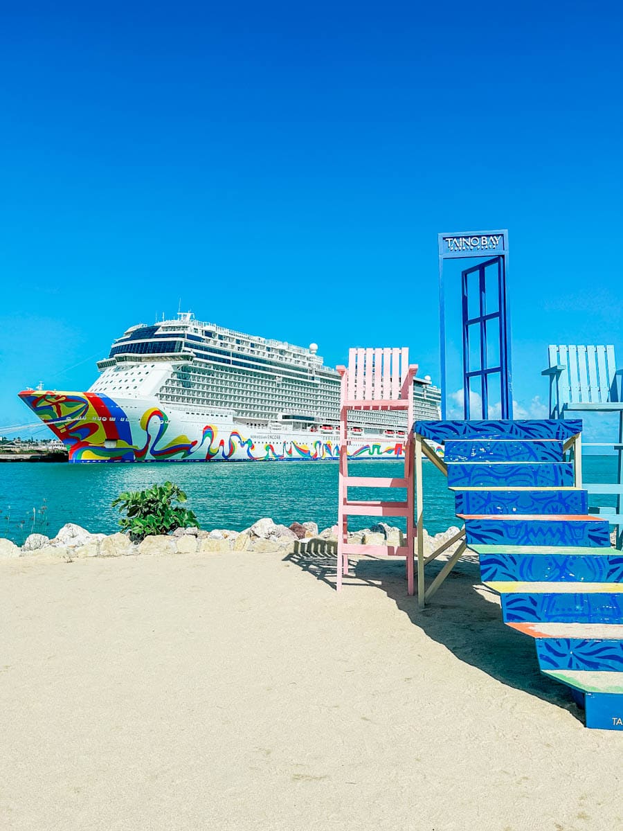Cruise ship with a brightly painted hull docked at Taino Bay in Puerto Plata, with colorful beach chairs on the sand