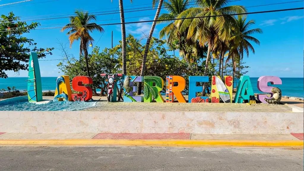 Colourful LAS TERRENAS letter sign on the seafront, with palm trees and the sea behind